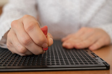 A woman uses a special stencil and stylus to write a letter in braille. 