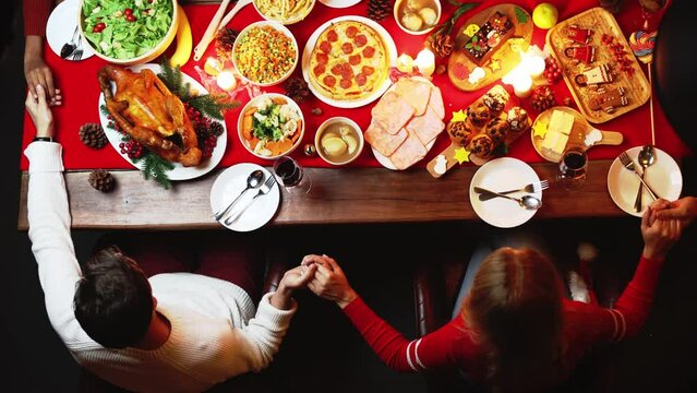 Groups of people celebrate Christmas eve and have dinner at night which have many food and wine on the table. A child give a present  box to grandparents.