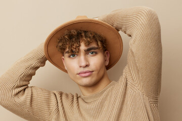 a handsome young man stands on a beige background in a stylish sweater with a hat on his head and...
