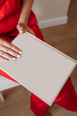 Book mock-up in hands of a woman. Album with clean cover. Book with a cover of cream textile. Empty book template. Young woman in red suits holds the empty book in her hands close-up. 