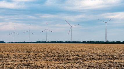 A row of windmills (wind turbines with rotating blades) against the backdrop of autumn field. Adyghe wind farm from many towers of wind turbines. Wind power complex of Rosatom.