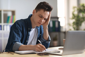 Young male entrepreneur massaging temple, suffering headache at workplace in office