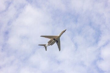 A portrait of a private plane flying low in a cloudy sky. The jet plane has started to descend for landing and the wheels are out.