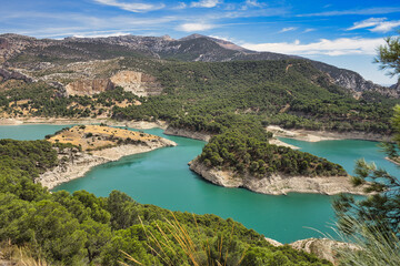 Obraz premium Spectacular panoramic views of the Guadalhorce reservoir, next to the Caminito del Rey in Malaga, Spain. Turquoise blue water and forest with blue sky on a sunny day.