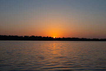 Sunset over a wide river or lake. Forest on the horizon and clear sky. Orange and blue