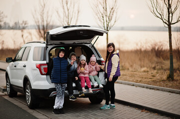 Mother with four kids sitting in trunk of big suv car.