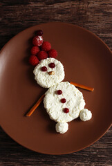 snowman made of cottage cheese and raspberries and lingonberries on a brown plate on a wooden...