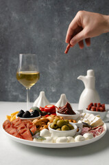 Classic italian antipasti or tapas  white wine snacks set. Cheese variety, black and green olives, pickles, prosciutto di Parma, tomatoes, salami, tarallini, man hand taking  the chorizo. Copy space 