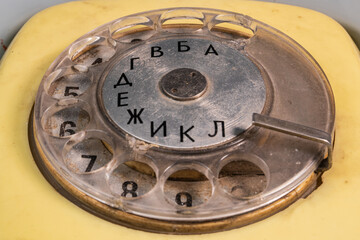 Dialing disc of an old yellow telephone with round holes and numbers. Macro shot of retro rotary...