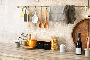 Kitchen utensils and utensils on a wooden countertop. Stylish kitchen interior. Wooden kitchen utensils hanging on metal railing. Ceramic plates, dishes and cozy decor on table	