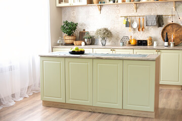 Modern home decor. Kitchen utensils, dishes and plates. Kitchen island in dining room. Green wooden kitchen interior with wooden shelf and cozy decoration. Stylish cuisine with flowers in vase.	