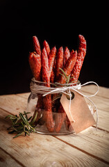 Polish kabanosy sausages in a jar. Thin dry sausages with blank label in a rural, eco composition, on black background.