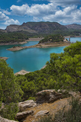 Spectacular panoramic views of the Guadalhorce reservoir, next to the Caminito del Rey in Malaga, Spain. Turquoise blue water and forest with blue sky on a sunny day.