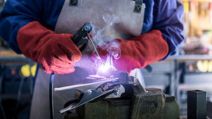 Skillful metal worker working with arc welding machine in factory. Sparks fly