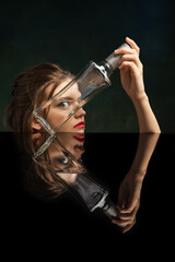 Conceptual art photography. Young girl's face through empty glass bottle over dark background....