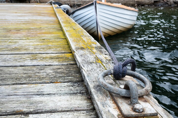 Iron mooring ring on an old wooden pier, a sailboat is knotted in the background.