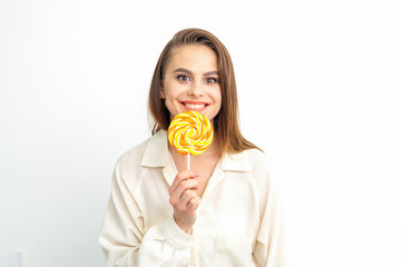 Beautiful young caucasian woman wearing a white shirt licking a lollipop on a white background