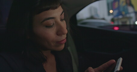 Female passenger typing message on smartphone in taxi backseat. Young woman using cellphone commuting from work at night