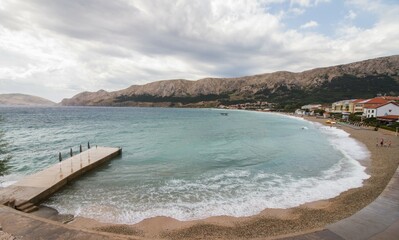 Beach of Baska, Krk, Croatia, on a cloudy day with waves and mountains 