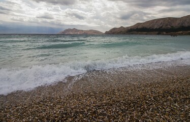 Beach of Baska, Krk, Croatia, on a cloudy day with waves and mountains 