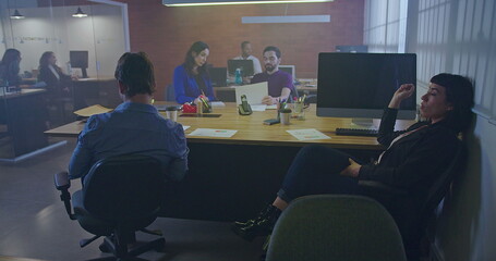 People working at Office workplace interior at night. Interior of busy employees in a coworking space. Corporate businessmen and businesswomen