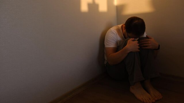 alone depressed man sitting in corner dark room because of problem and sadness in life. Sadnes and spite concept.