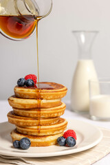 food photo of a stack of pancakes decorated with fruit on which syrup is poured