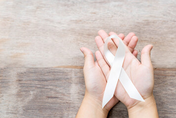 White ribbon on two hand in wooden background.