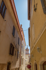 Narrow street with typical mediterranean buildings, church and blue sky at Krk, island of Krk, Croatia