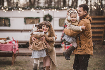 happy family of four: mom, dad and twin sisters celebrate Christmas near trailer with New Year...