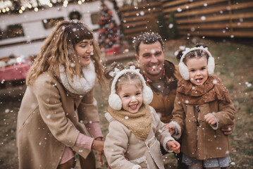 happy family of four: mom, dad and twin sisters celebrate Christmas near trailer with New Year decorations. Stylish family in fur coats and sheepskin coats is having fun in the snow. Selected focus