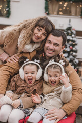 happy family of four: mom, dad and twin sisters celebrate Christmas near trailer with New Year decorations. Stylish family in fur coats and sheepskin coats is having fun in the snow. Selected focus