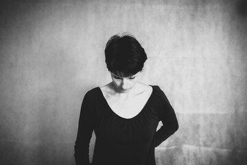 Schwarz-Weiß-Porträt einer schönen Frau auf dunklem Hintergrund, steht allein mit gesenktem Kopf