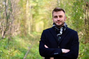 Handsome guy in a black coat in the forest. Cute guy with stubble and a model hairstyle is posing...