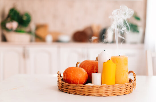 Pumpkins and extinguished candles with smoke on a wooden table against the background of the kitchen. The autumn image of the season, a cozy home atmosphere.