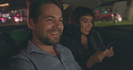 Happy carefree people in taxi backseat commuting from work at night. Smiling person in moving car