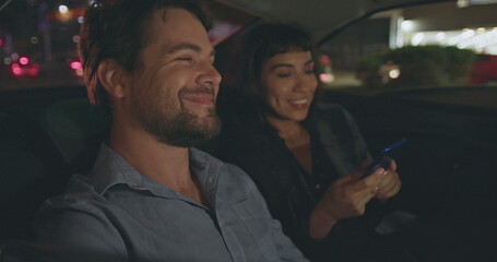 Young man and woman riding taxi in backseat after work at night. Male passenger looking out car window staring at nightlife city street. People riding cab