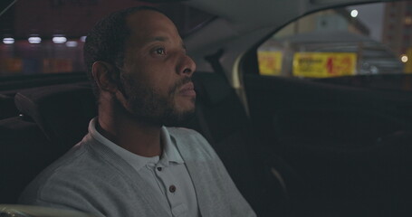 A black man seated in car backseat commuting from work at night. African American person riding taxi cab in the evening