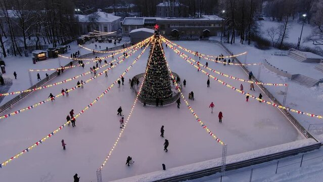 Festive ice rink with people skating around Christmas tree