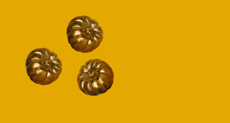 Three small gold pumpkins on yellow background. Levitation autumn, halloween concept. Place for text.