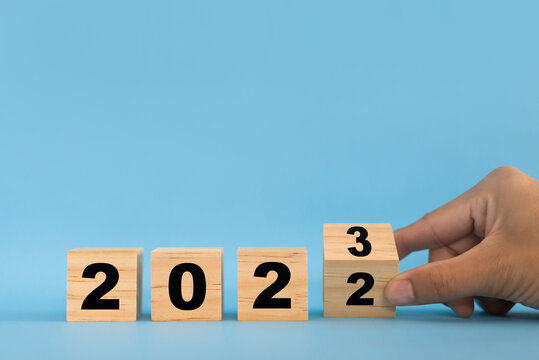 Hand flipping wooden blocks on blue background for change year 2022 to 2023. Setting goals for the upcoming new year.