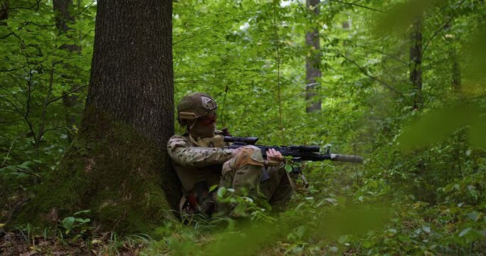 Ukrainian military sniper runs through the forest and takes cover behind a tree and reloads his rifle. overall plan