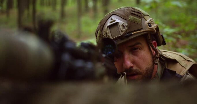 a sniper in ammunition and a helmet lies on a zeppelin in litsya and aims at an optical sight with one eye closed. bearded soldier aims with weapons in the forest. close-up
