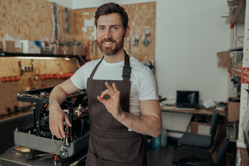 Repairman standing on workshop of coffee machines warehouse and show ok sign