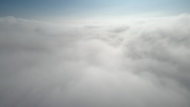 Aerial shot of flying over a layer of soft clouds at dawn