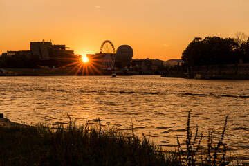 Sunset on the Vistula river in Krakow. Sun hides behind buiding and big wheel.