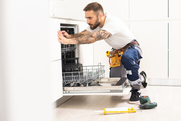 Young Repairman Service Worker Repairing Dishwasher Appliance In Kitchen