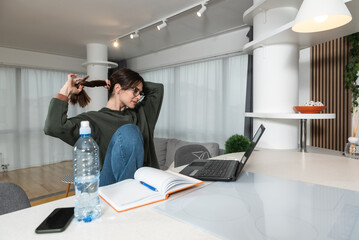 Young college student doing homework at home on her laptop. Girl reading and doing research for her...