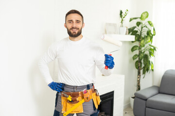 Close-up of person painter holding roller covered in blue paint. Professional worker wearing protective uniform and gloves. Copy space in right side. Renovation concept.