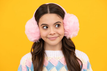 Modern teen girl wearing sweater and winter warm earmuff ear-flaps hat on isolated yellow background.